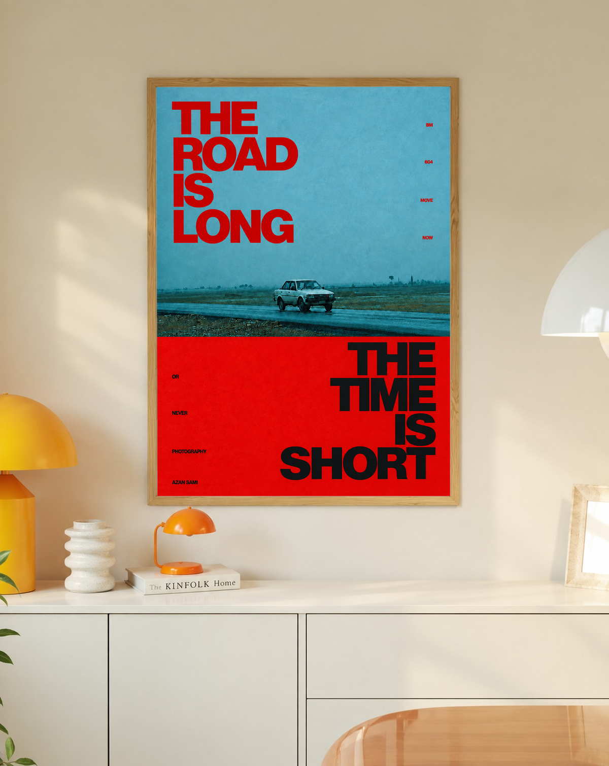 A small vintage car between blue and red blocks with bold road and time lettering in a slim oak frame on a cream wall above a white cabinet