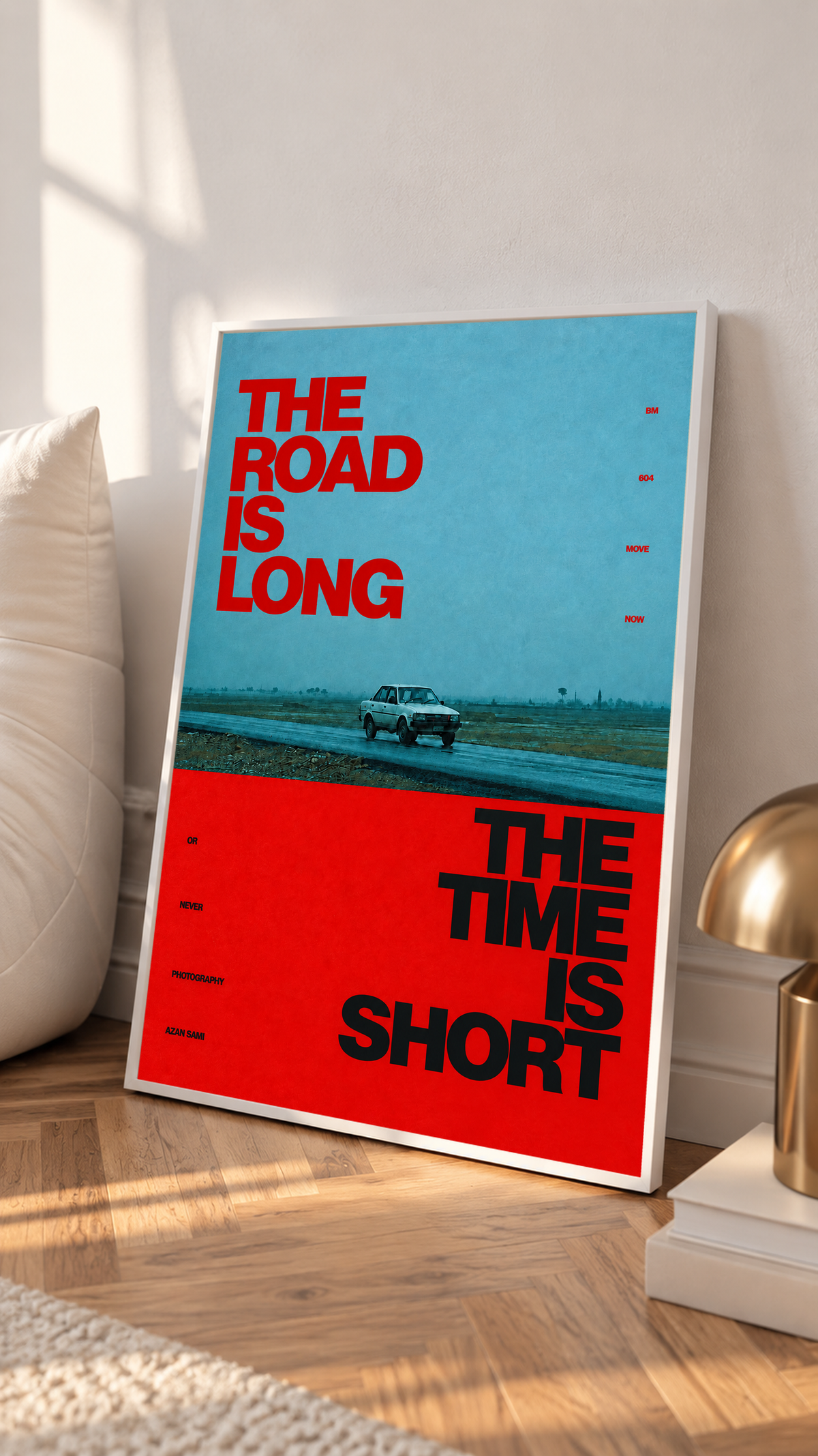 A small vintage car between blue and red blocks with bold road and time lettering in a white frame on a sunlit floor beside a white cabinet