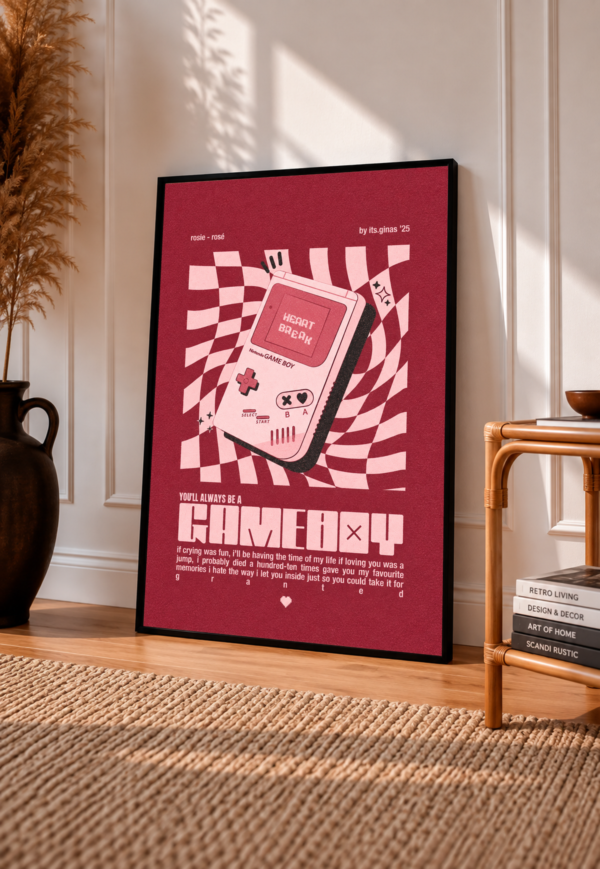 A pink Game Boy-style console with Heart Break screen on a wavy pink checkerboard in a black frame leaning on a sunlit floor beside a rattan chair