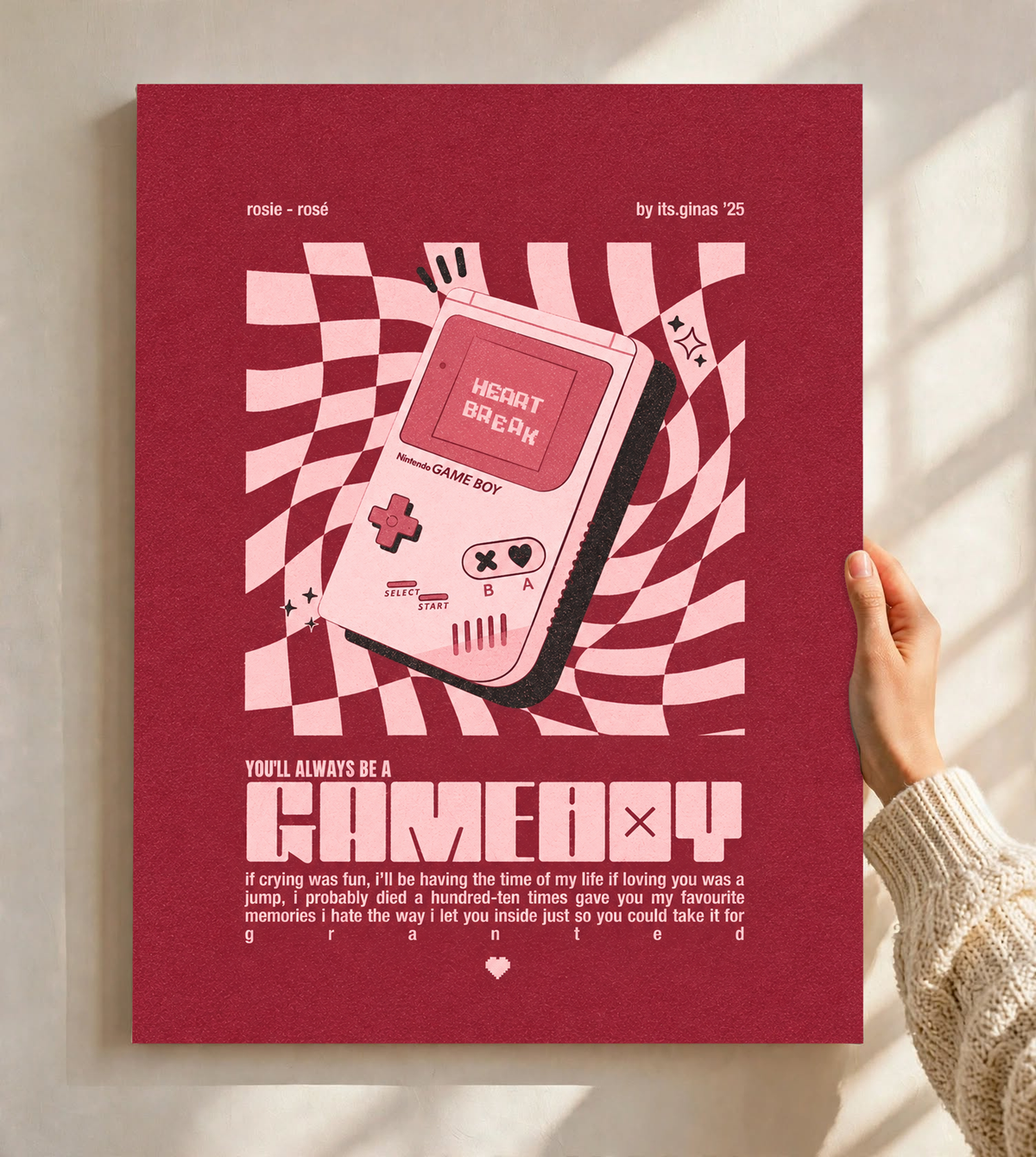 A pink Game Boy-style console with Heart Break screen on a wavy pink checkerboard as an unframed poster held against a pale sunlit wall