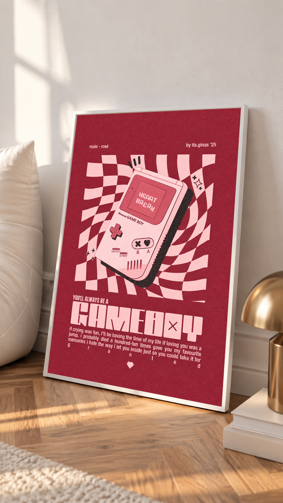A pink Game Boy-style console with Heart Break screen on a wavy pink checkerboard in a white frame on a sunlit floor beside a white cabinet
