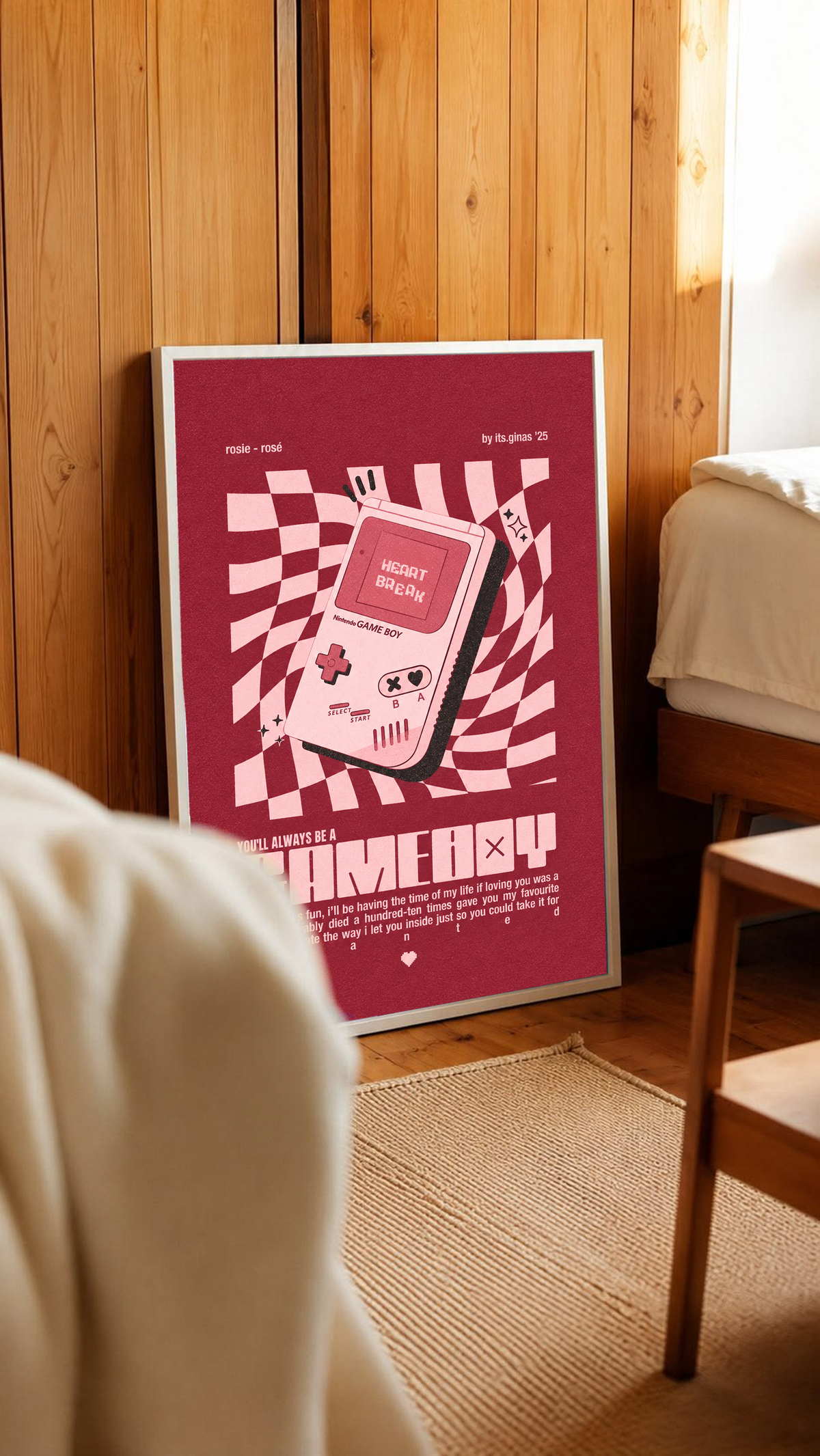 A pink Game Boy-style console with Heart Break screen on a wavy pink checkerboard in a white frame leaning against warm wooden wall panels