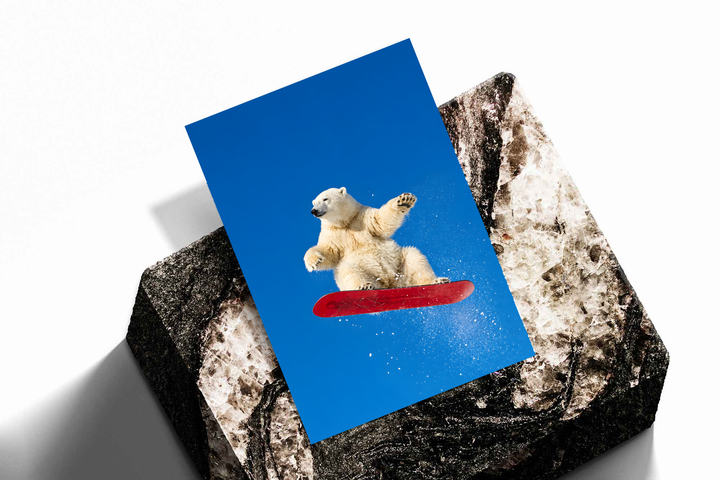 White polar bear airborne on a red snowboard with scattered snow against a bright blue sky, shown as an unframed print tilted on a dark stone display against a light background