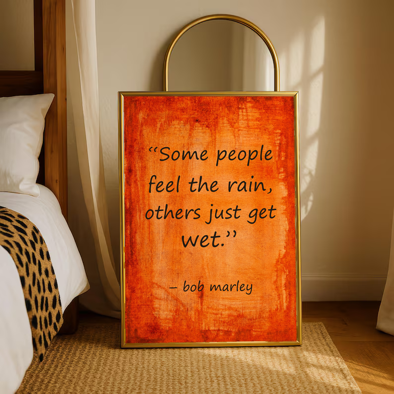 Standing framed quote poster on orange textured background reading “Some people feel the rain”