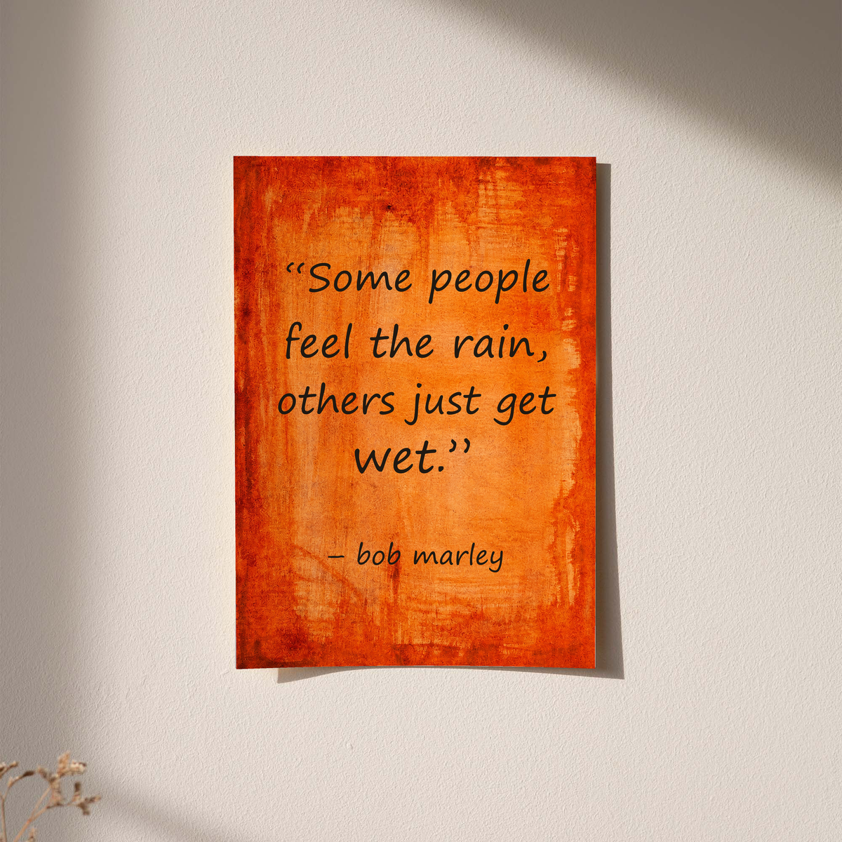 Wall-hung framed quote poster with orange textured background and “Some people feel the rain”