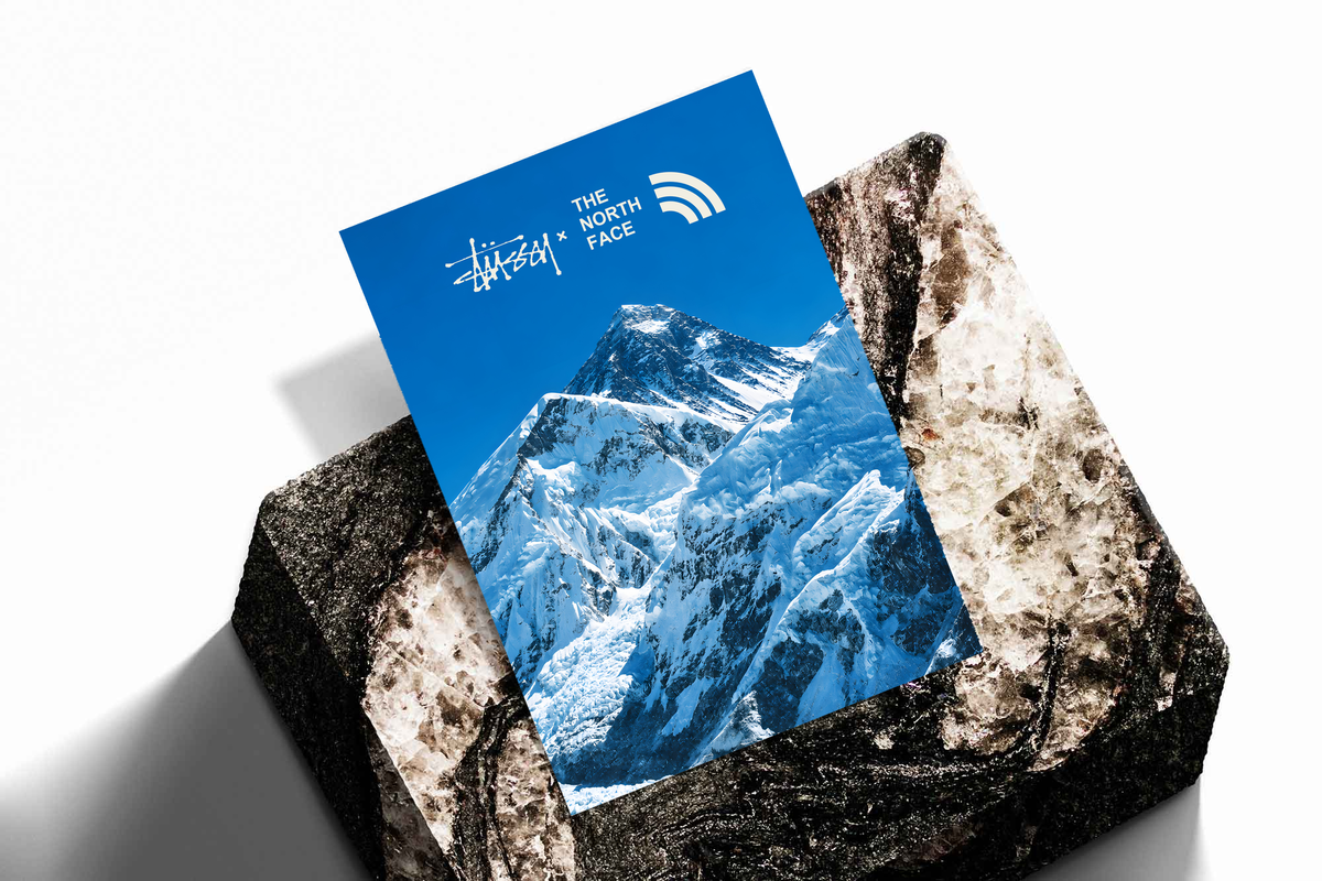 Blue snowy mountain landscape with Stussy and The North Face marks; unframed print on a stone display