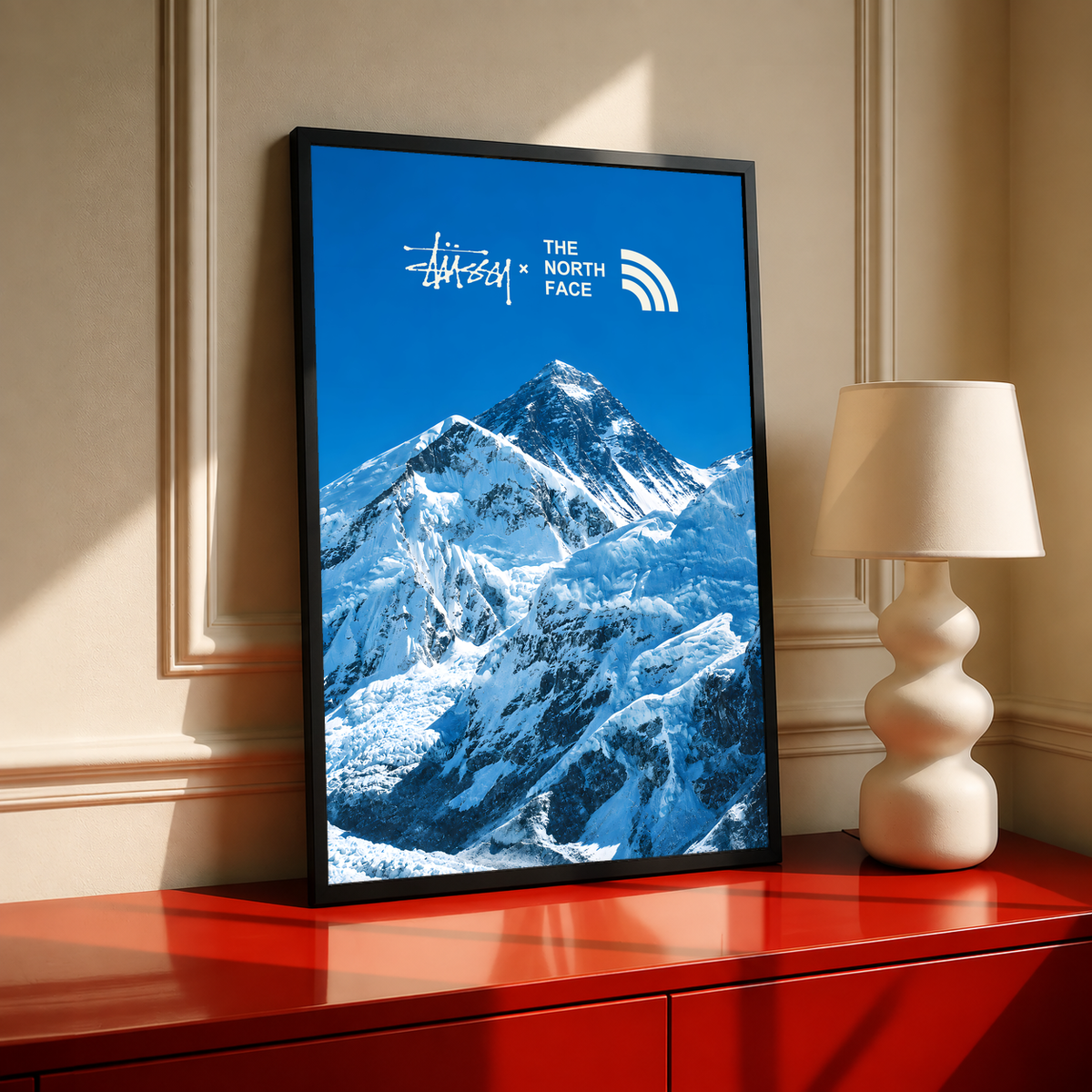Blue snowy mountain landscape with Stussy and The North Face marks; black framed print on a red cabinet