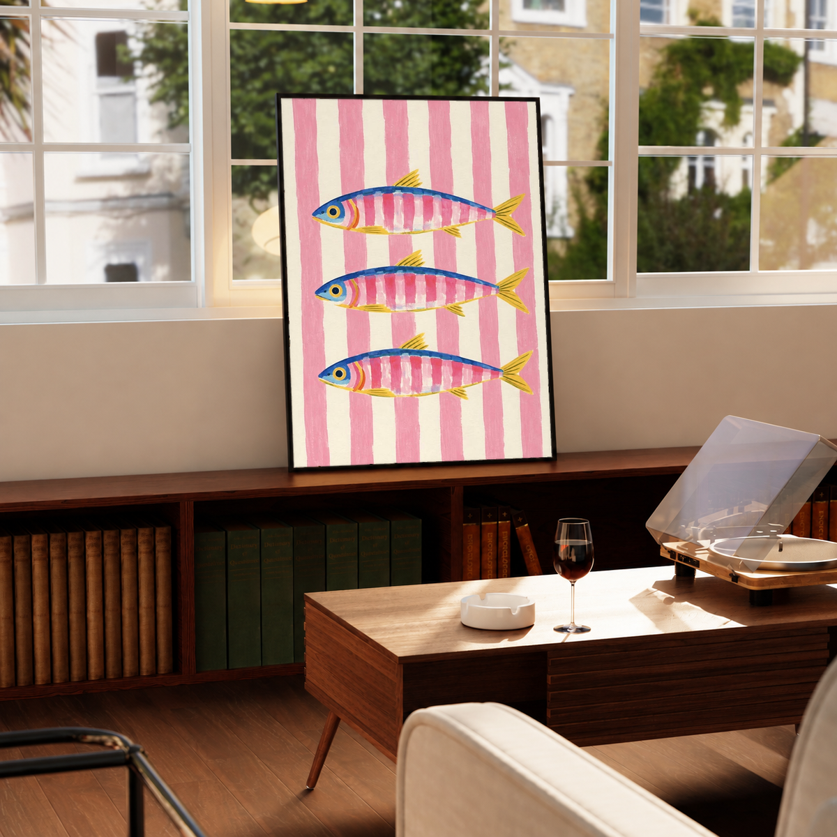 Framed vertical art print with three fish on pink vertical stripes, on a wooden table