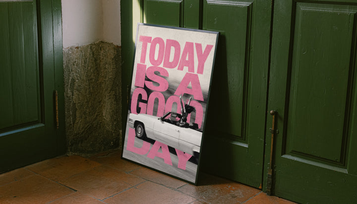 Bold pink TODAY IS A GOOD DAY lettering behind a black-and-white convertible car collage leaning on the floor against dark green wall panelling