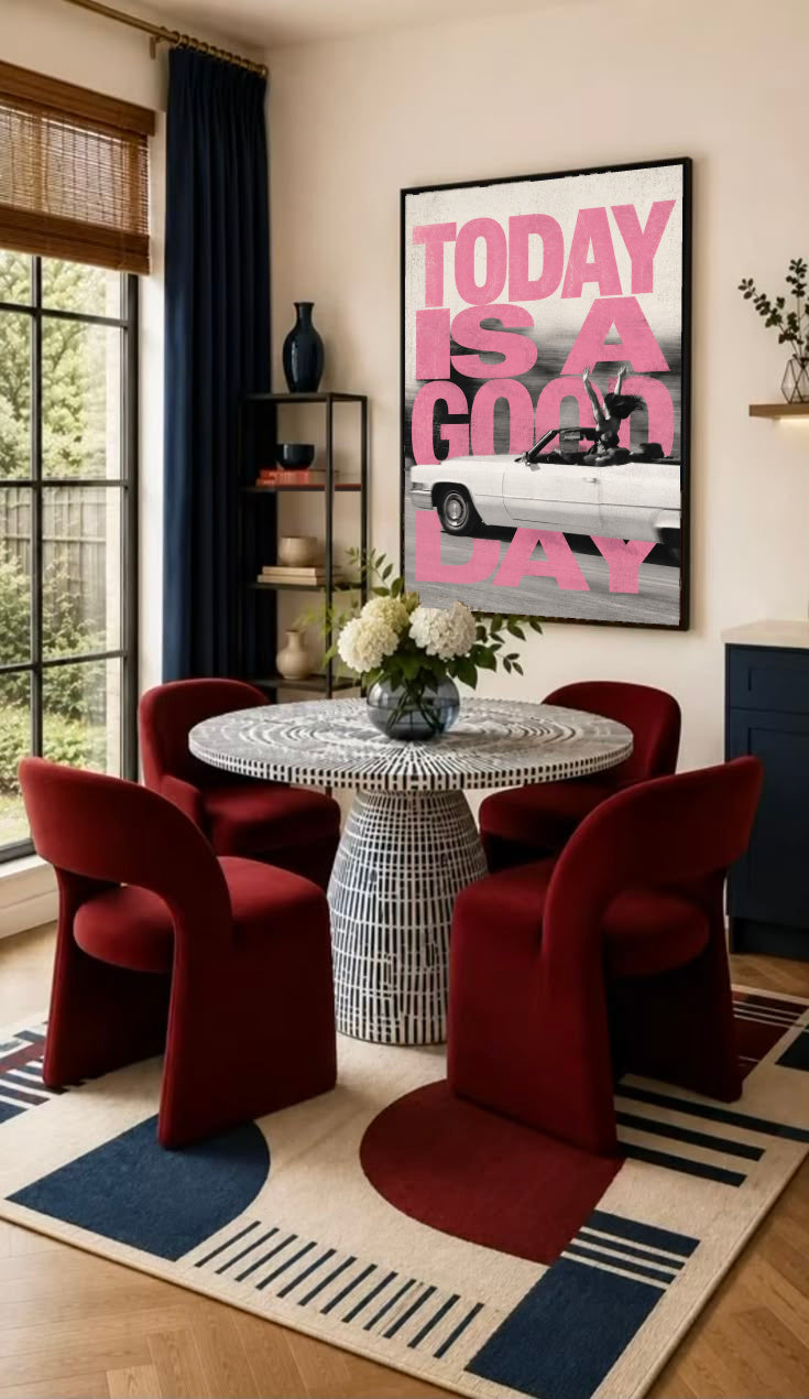 Bold pink TODAY IS A GOOD DAY lettering behind a black-and-white convertible car collage in a black frame on the wall of a dining nook with red chairs