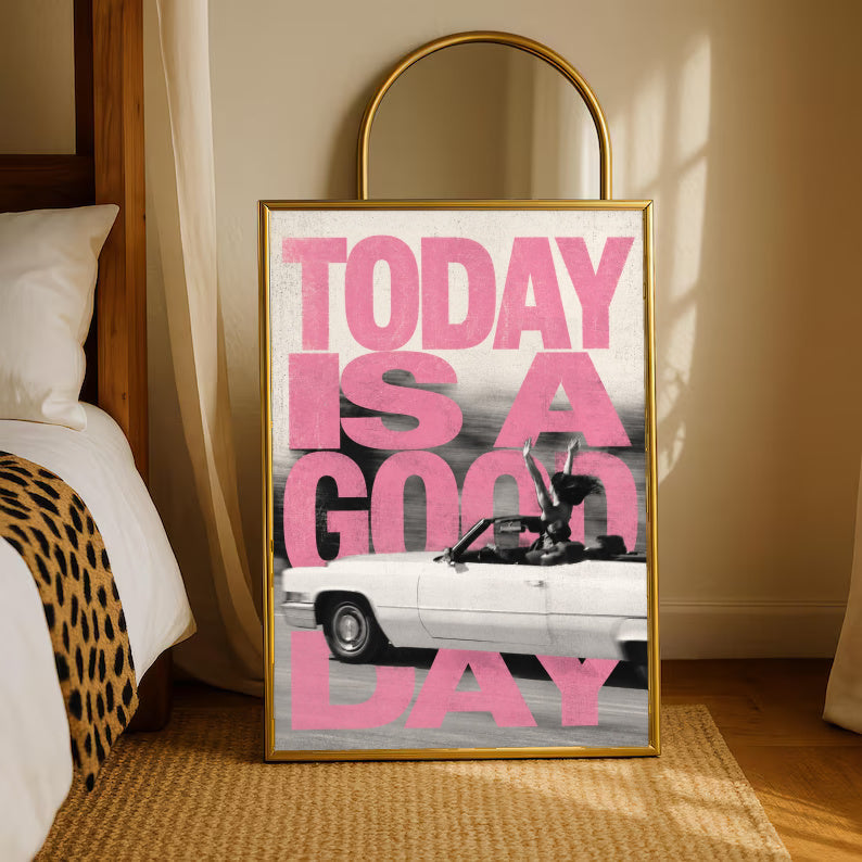 Bold pink TODAY IS A GOOD DAY lettering behind a black-and-white convertible car collage in a gold-tone styling frame leaning beside a bedroom mirror