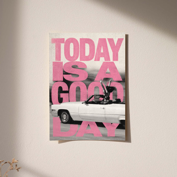 Bold pink TODAY IS A GOOD DAY lettering behind a black-and-white convertible car collage displayed without a visible frame on a softly lit pale wall