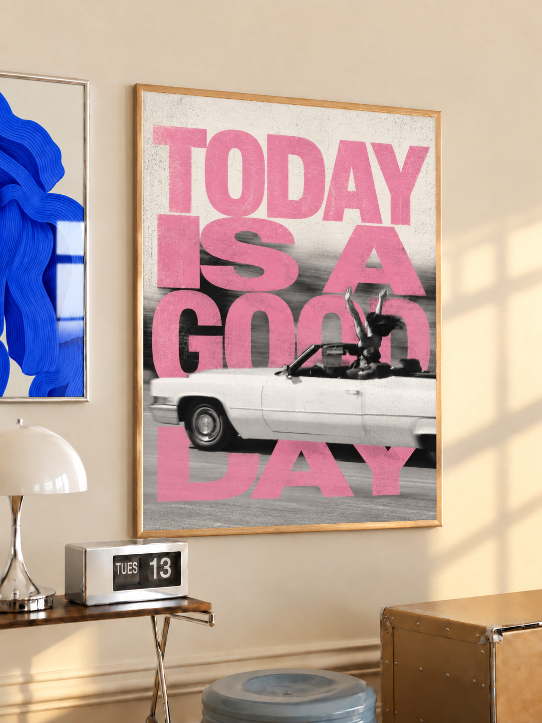 Bold pink TODAY IS A GOOD DAY lettering behind a black-and-white convertible car collage in a light wood frame on a sunlit office wall beside a desk