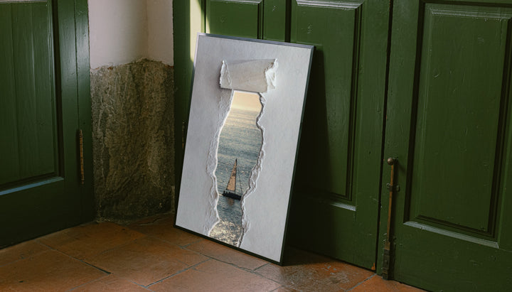 A sailboat at sea seen through a printed torn-paper opening on a grey ground leaning on the floor against dark green wall panelling
