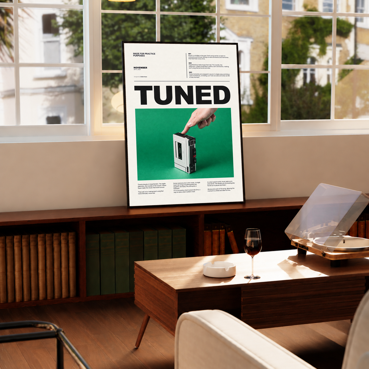 A hand pressing a portable cassette player against green beneath Tuned typography in a black frame by a bright window above a record player