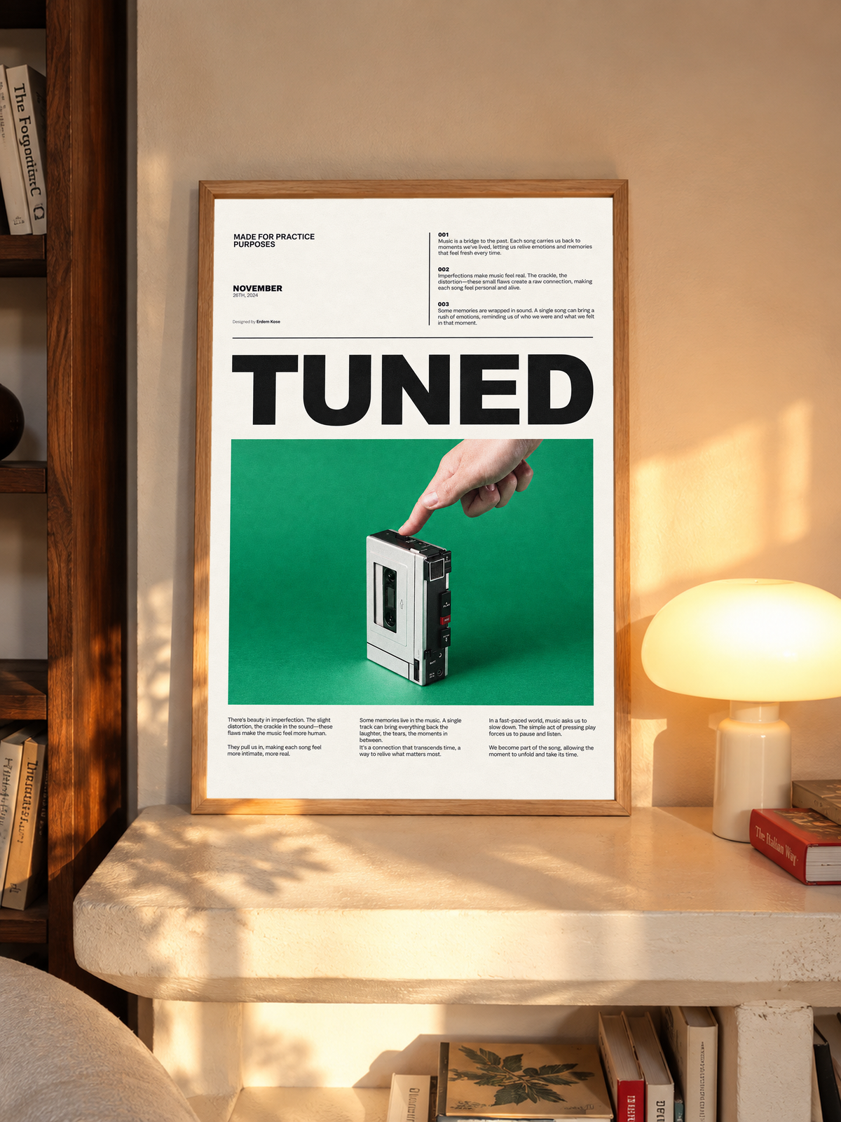 A hand pressing a portable cassette player against green beneath Tuned typography in an oak frame above a pale wooden sideboard beside a glowing lamp