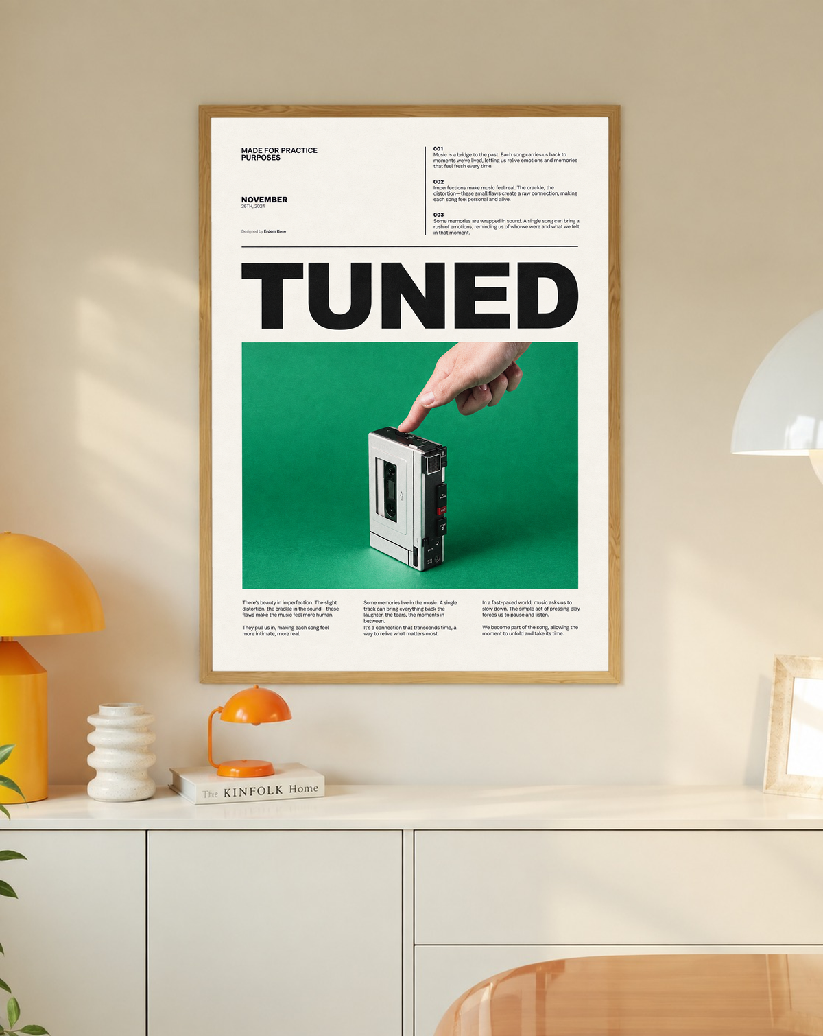 A hand pressing a portable cassette player against green beneath Tuned typography in a slim oak frame on a cream wall above a white cabinet