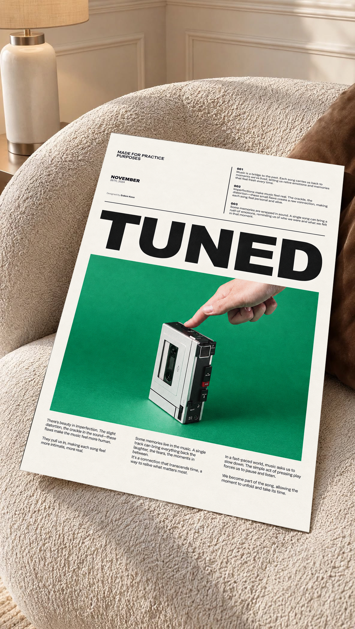 A hand pressing a portable cassette player against green beneath Tuned typography as an unframed poster resting on a cream woven chair