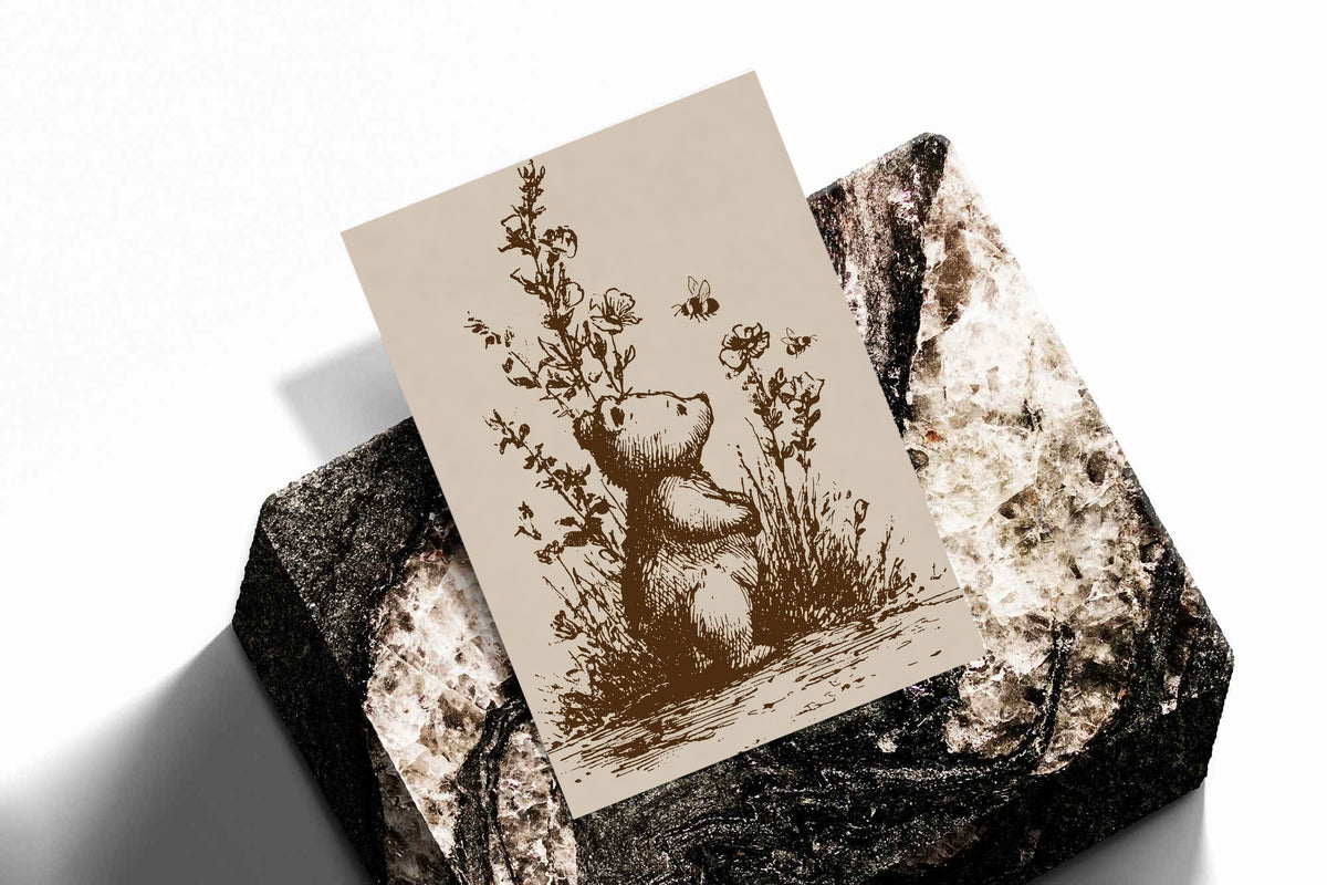 Vintage bear and bee art print with wildflower stems in sepia, leaning on textured surface.