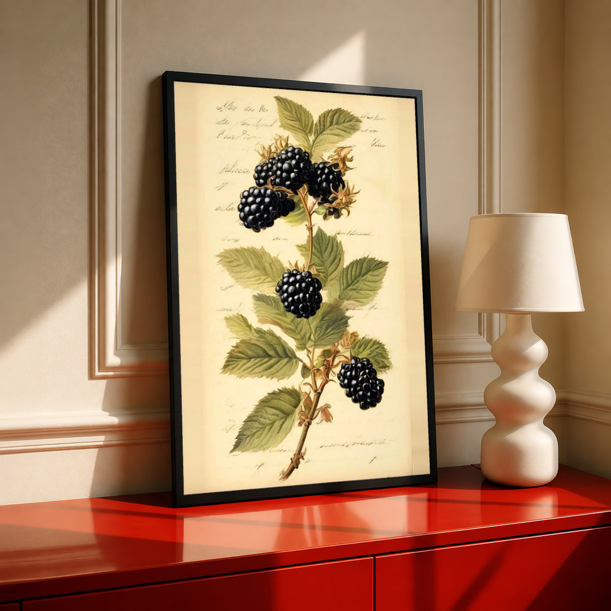 Dark blackberry clusters and serrated green leaves on a branch with notes on aged cream in a black frame on a red cabinet beside a cream lamp