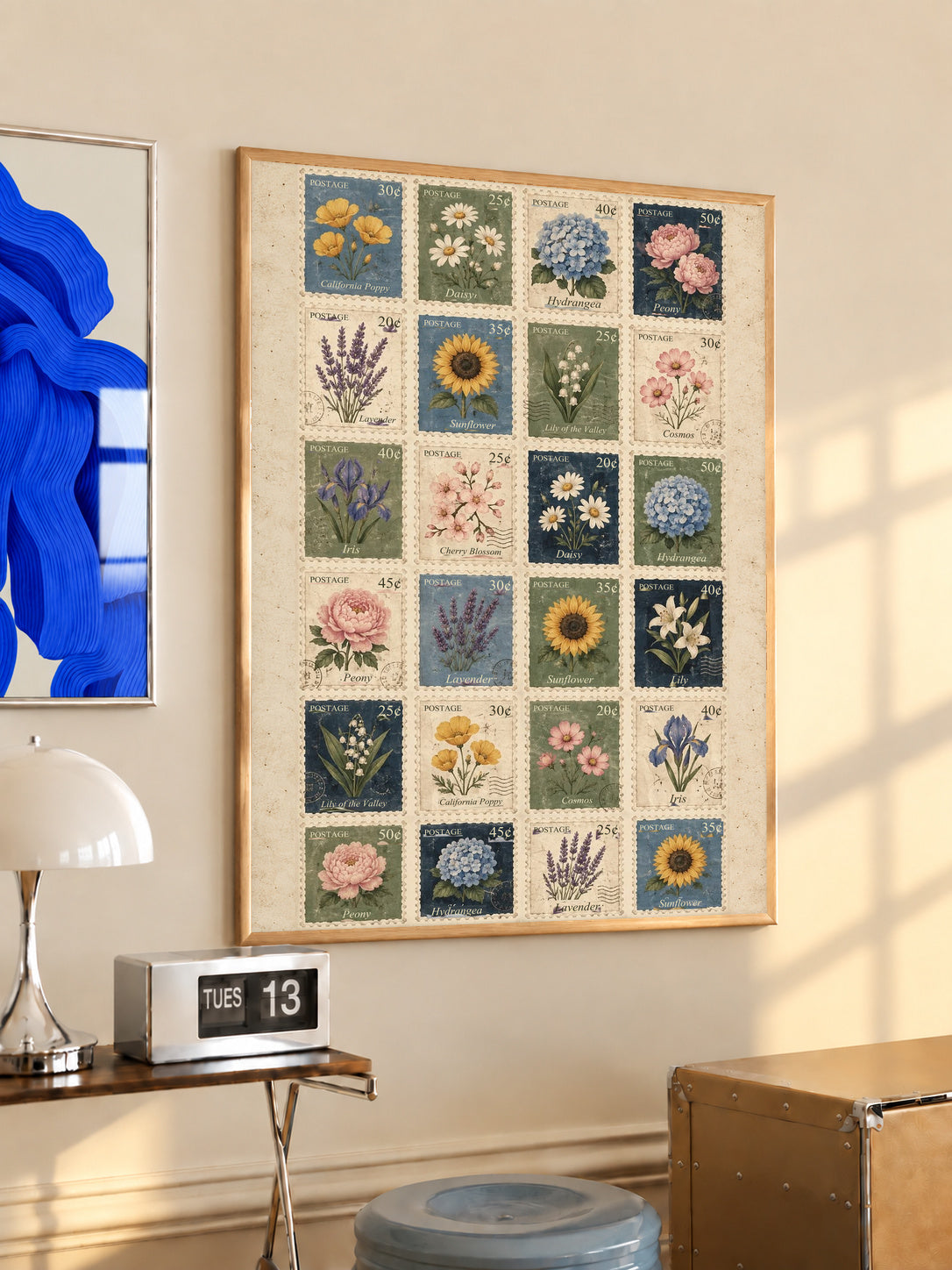 Grid of twenty four illustrated floral postage stamps in muted garden colours in an oak frame above a console beside a blue print and calendar