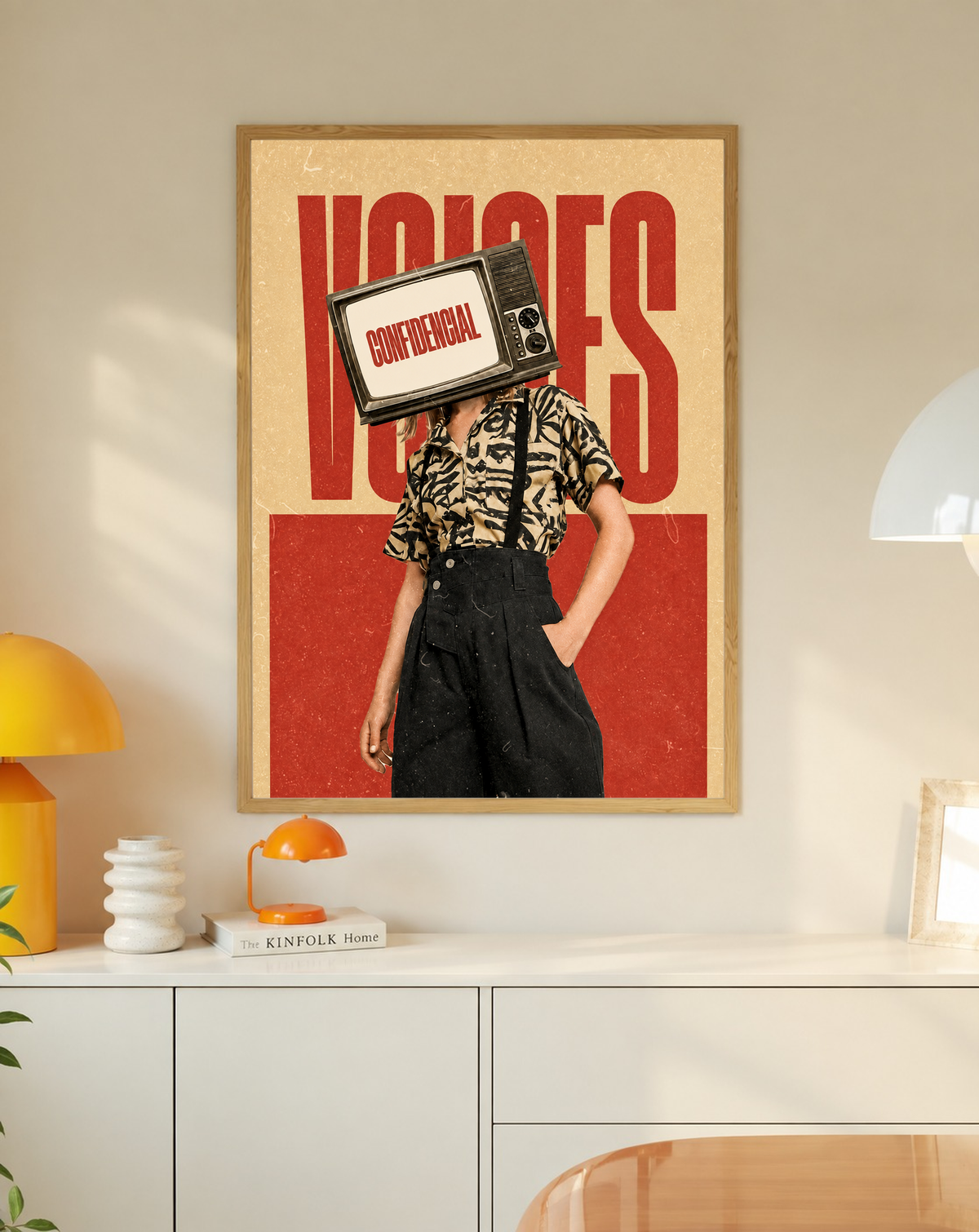 A television-headed figure in a patterned shirt before red Voices lettering in a slim oak frame on a cream wall above a white cabinet