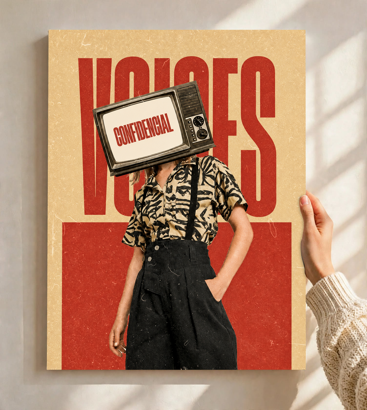 A television-headed figure in a patterned shirt before red Voices lettering as an unframed poster held against a pale sunlit wall
