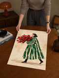 Watercolor art print on a table: woman in green striped dress holding red flower bouquet