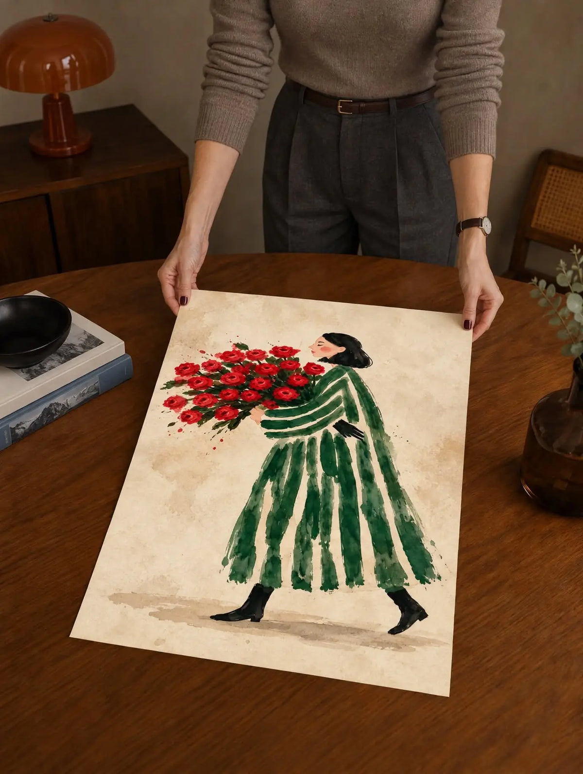 Watercolor art print on a table: woman in green striped dress holding red flower bouquet