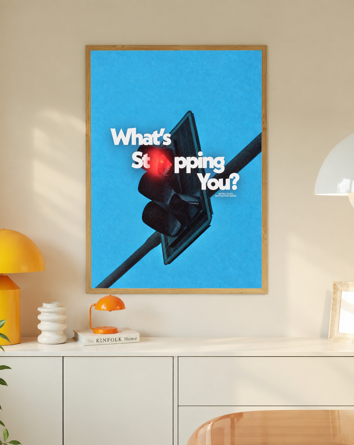 White What's Stopping You lettering over a red traffic light against blue sky in a slim oak frame on a cream wall above a white cabinet