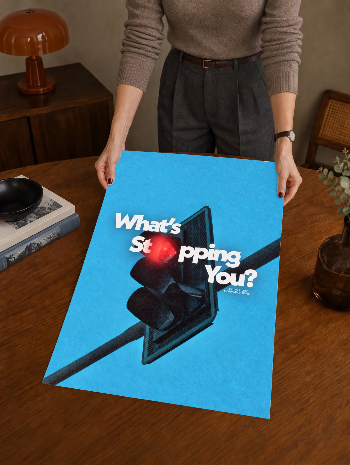 White What's Stopping You lettering over a red traffic light against blue sky as a large unframed poster held above a wooden desk