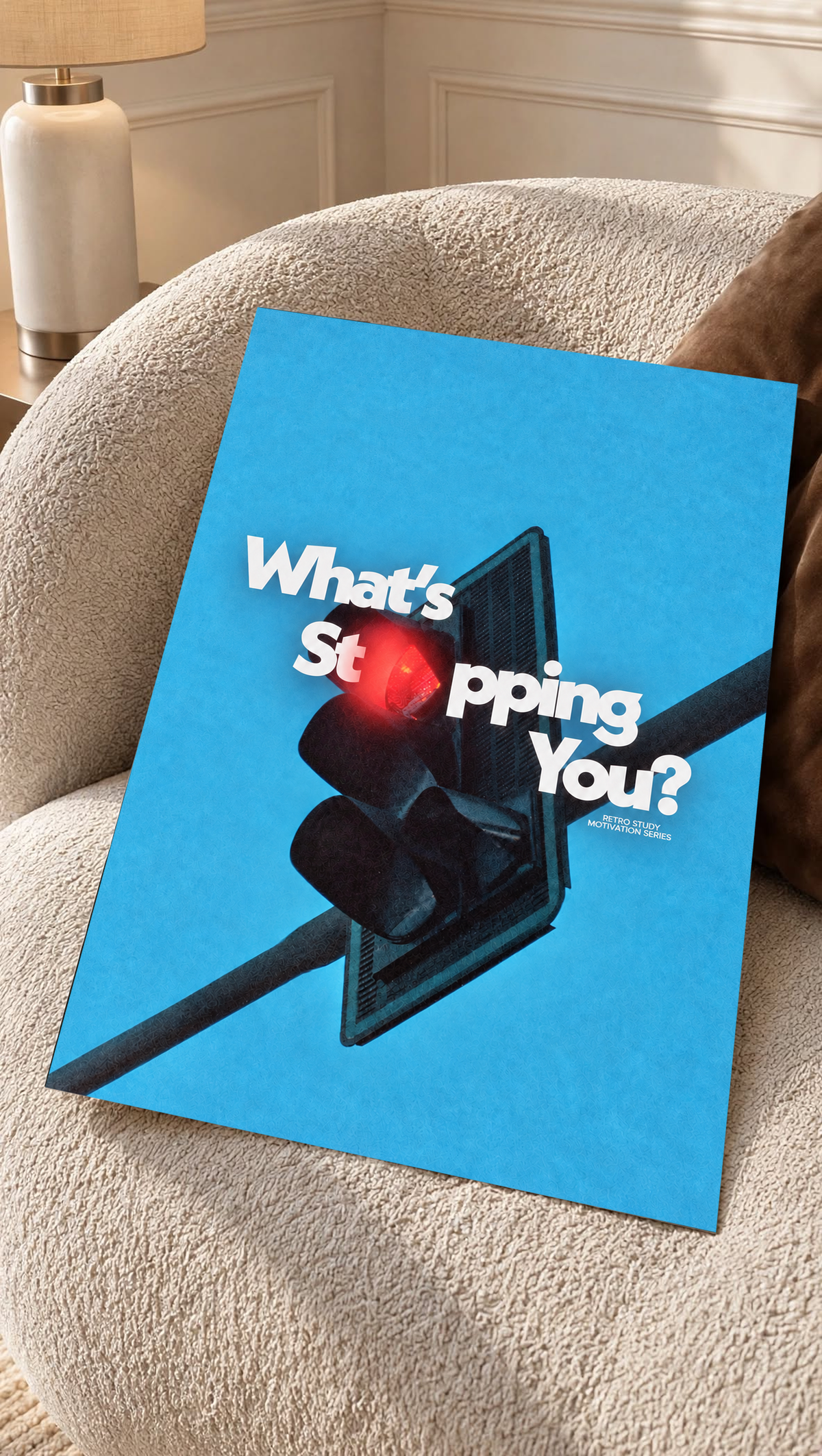 White What's Stopping You lettering over a red traffic light against blue sky as an unframed poster resting on a cream woven chair