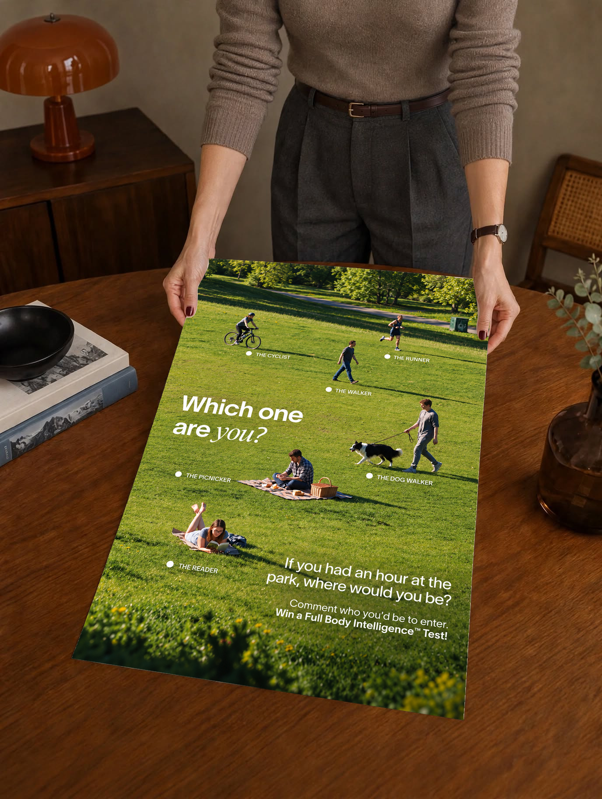 Six park activities labelled across a green lawn beneath Which One Are You text as a large unframed poster held above a wooden desk