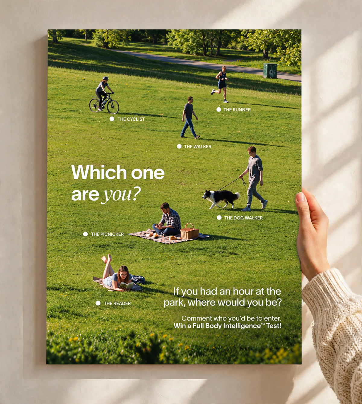 Six park activities labelled across a green lawn beneath Which One Are You text as an unframed poster held against a pale sunlit wall