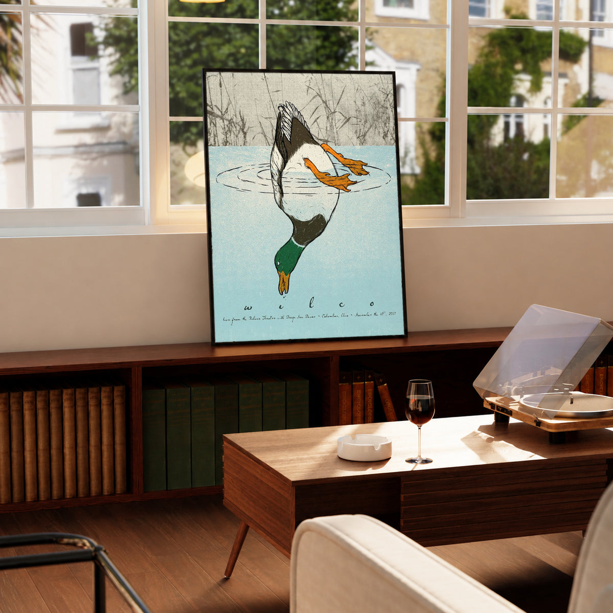 Black-framed diving duck art print with blue water on a wooden table by windows