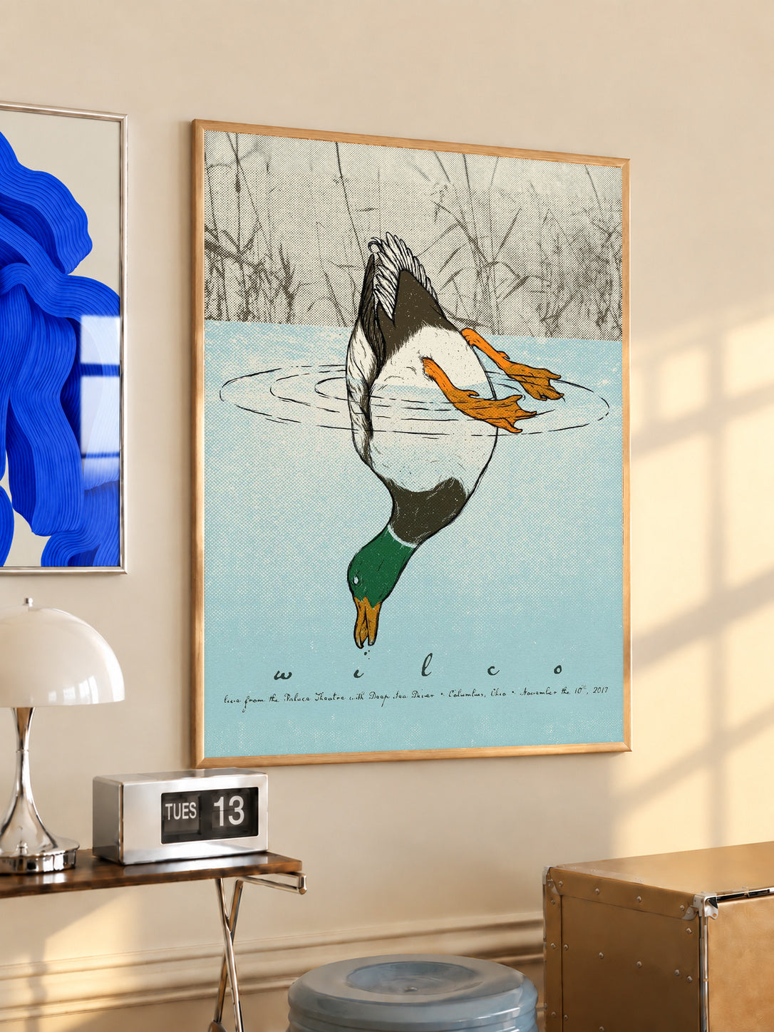 Wood-framed diving duck art print with blue water and orange ducks, hanging indoors
