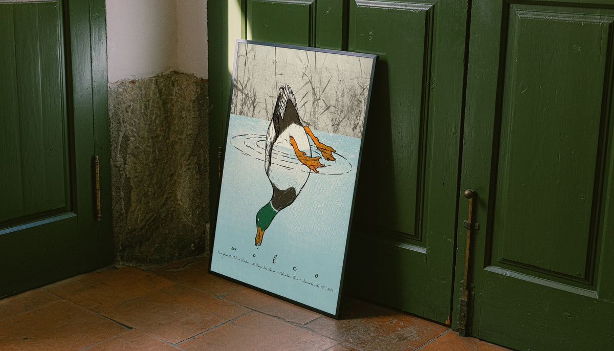 Black-framed diving duck art print leaning against a green door, blue water scene