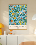 William Morris Fruit botanical pattern with yellow fruit and green leaves on pale blue in an oak frame on a wall above a white cabinet beside a yellow lamp