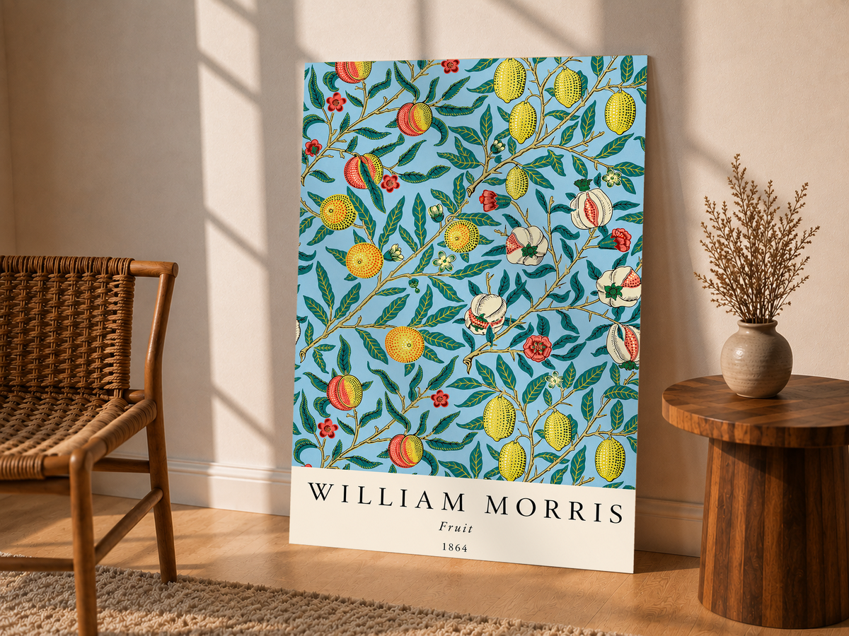 William Morris Fruit botanical pattern with yellow fruit and green leaves on pale blue as an unframed display leaning beside a wicker chair and side table