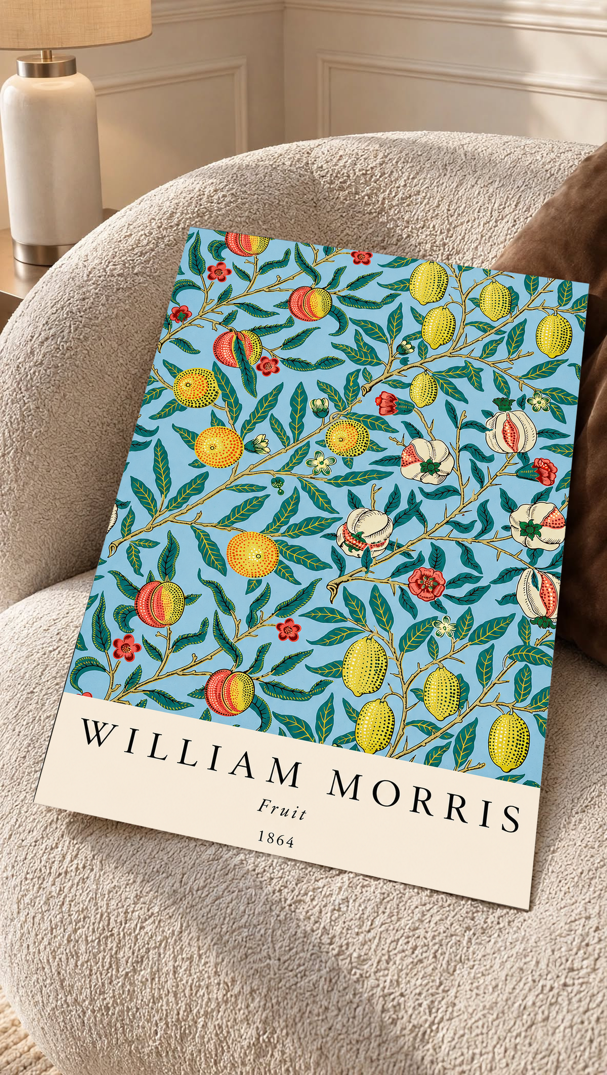 William Morris Fruit botanical pattern with yellow fruit and green leaves on pale blue as an unframed print resting on a boucle chair