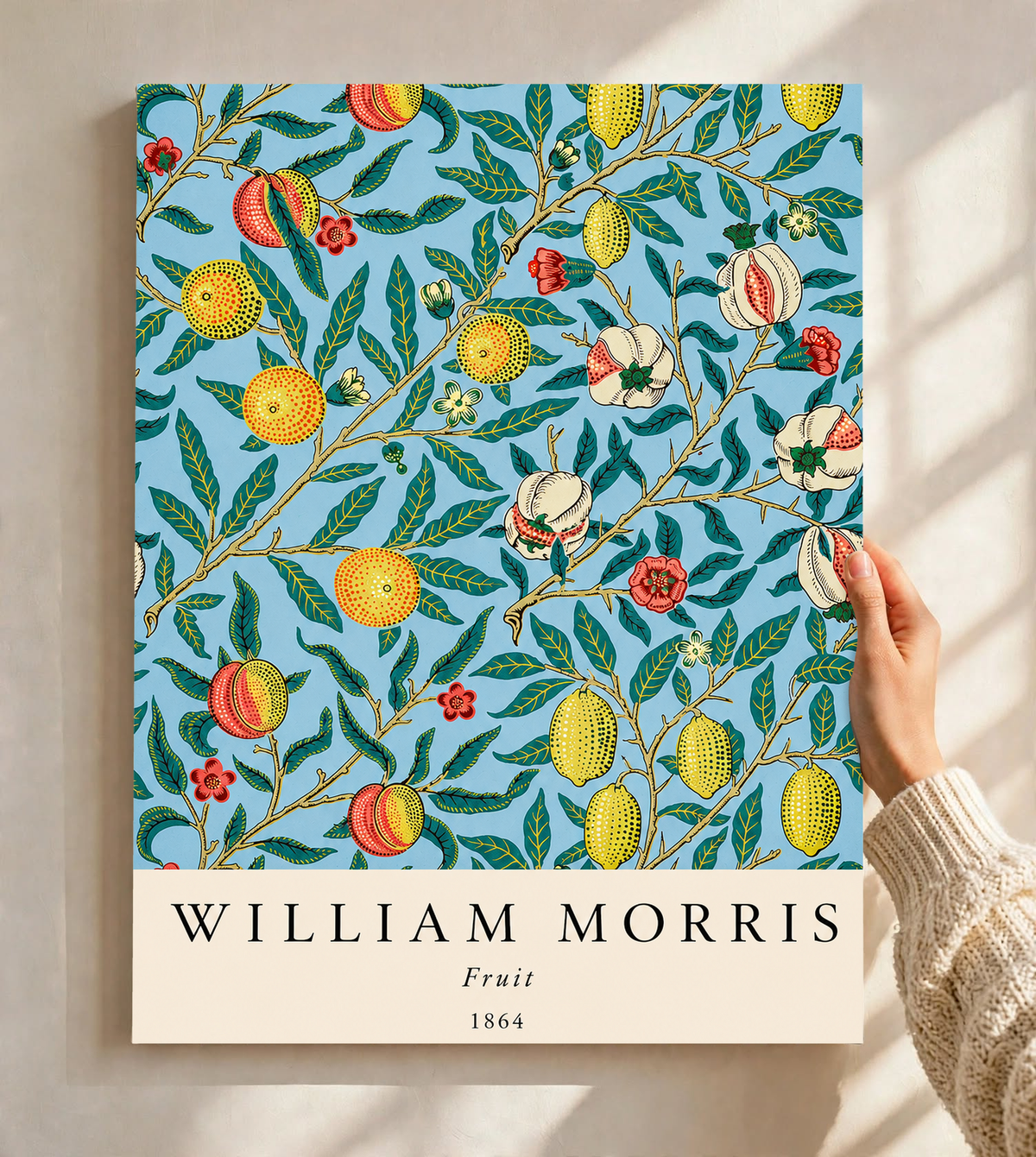 William Morris Fruit botanical pattern with yellow fruit and green leaves on pale blue as an unframed print held against a pale wall in a close view