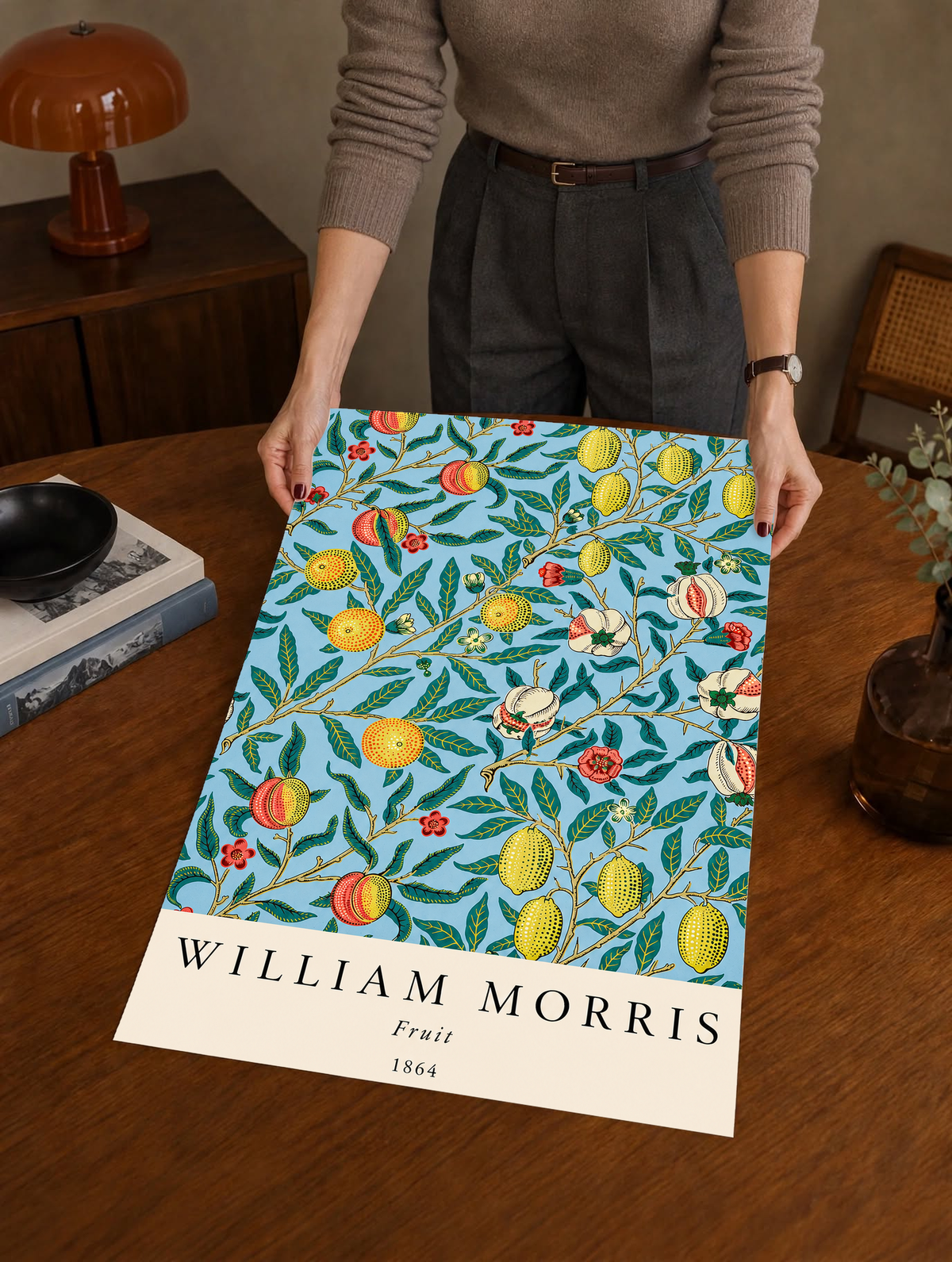 William Morris Fruit botanical pattern with yellow fruit and green leaves on pale blue as an unframed print held over a wooden table beside a record player