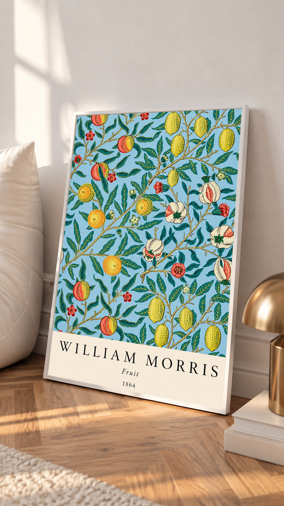 William Morris Fruit botanical pattern with yellow fruit and green leaves on pale blue in a white frame leaning on a sunlit floor beside a brass lamp