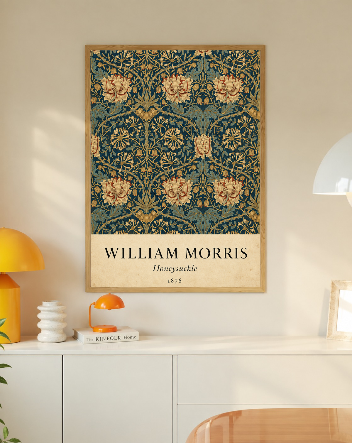 William Morris Honeysuckle floral pattern with gold and pink blooms on dark teal in an oak frame on a wall above a white cabinet beside a yellow lamp