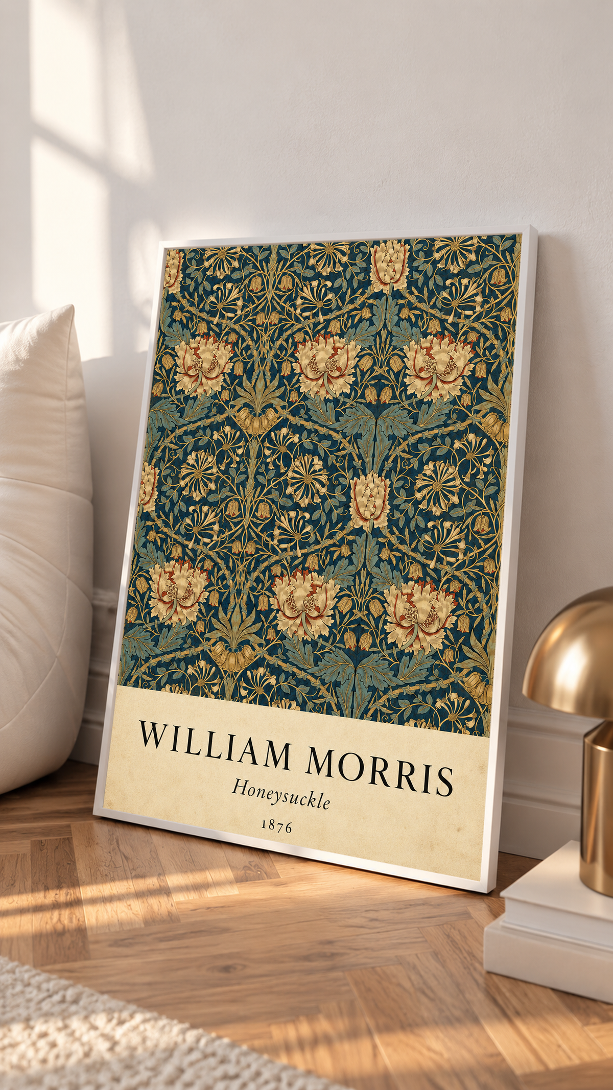 William Morris Honeysuckle floral pattern with gold and pink blooms on dark teal in a white frame leaning on a sunlit floor beside a brass lamp