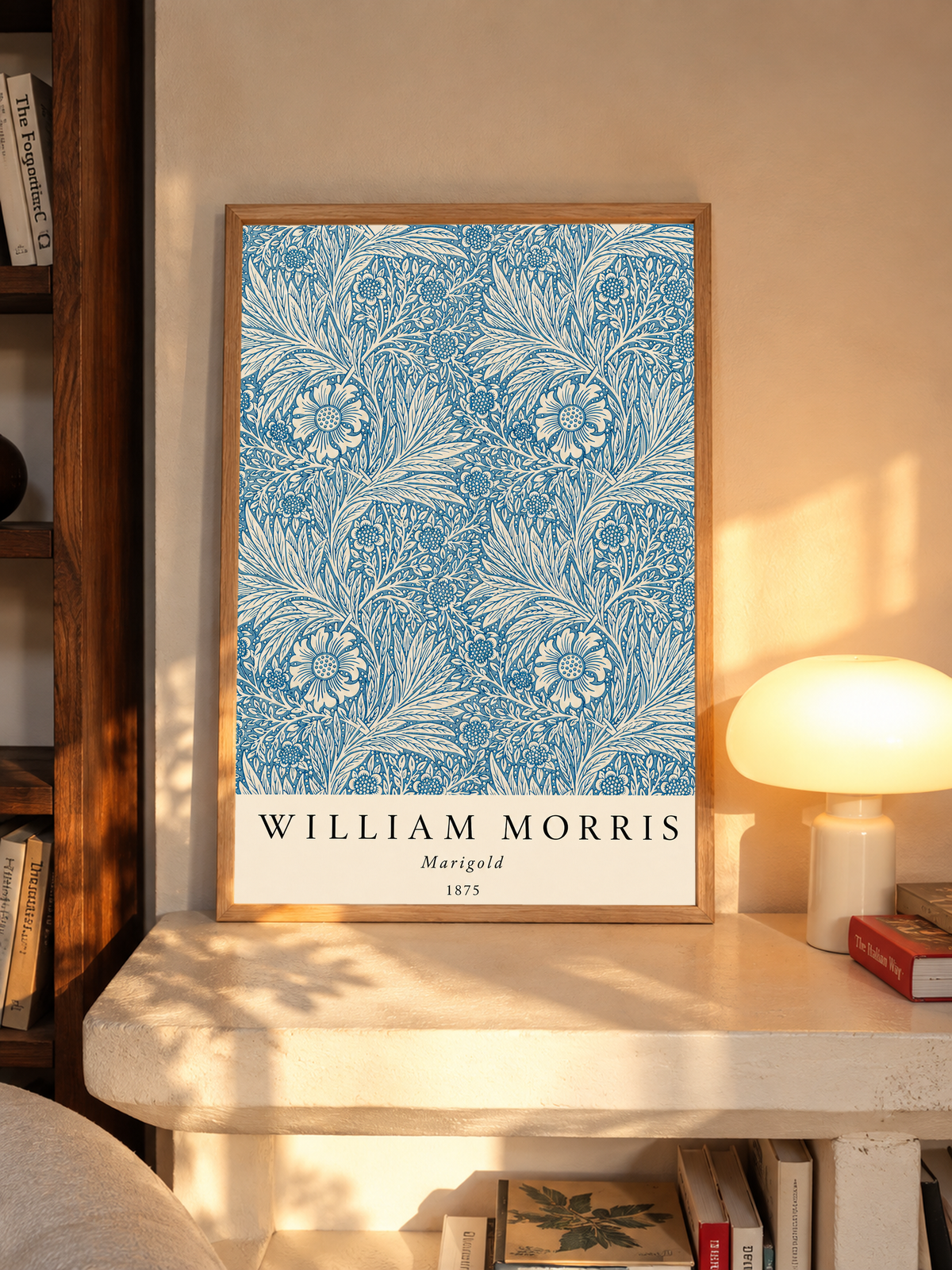 William Morris Marigold blue and cream floral leaf pattern in an oak frame on a sunlit console beside books and a cream lamp