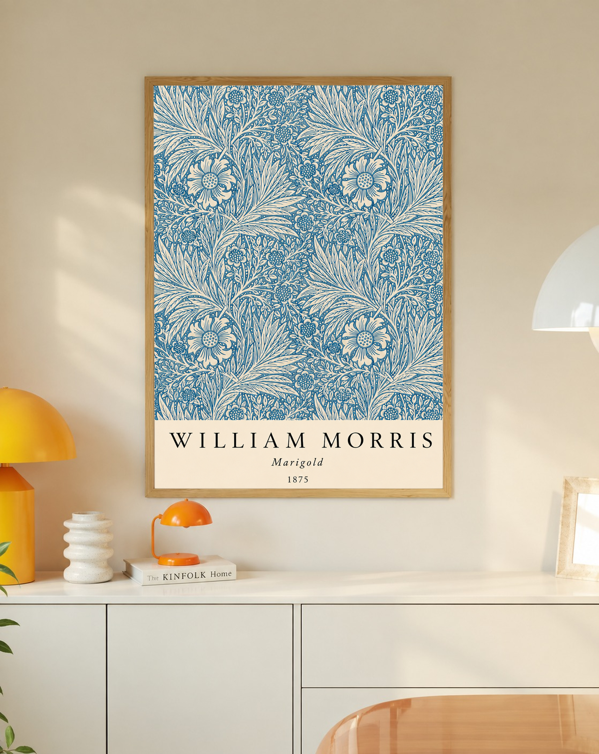 William Morris Marigold blue and cream floral leaf pattern in an oak frame on a wall above a white cabinet beside a yellow lamp