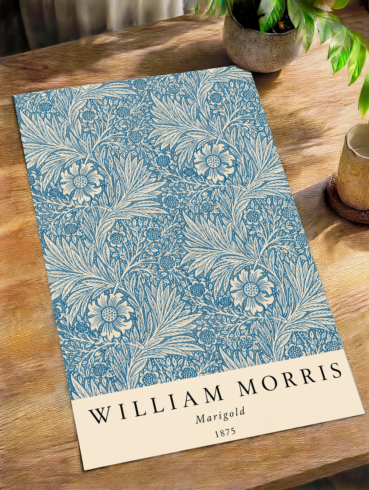 William Morris Marigold blue and cream floral leaf pattern as an unframed print on a wooden table beside a plant