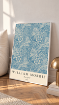 William Morris Marigold blue and cream floral leaf pattern in a white frame leaning on a sunlit floor beside a brass lamp