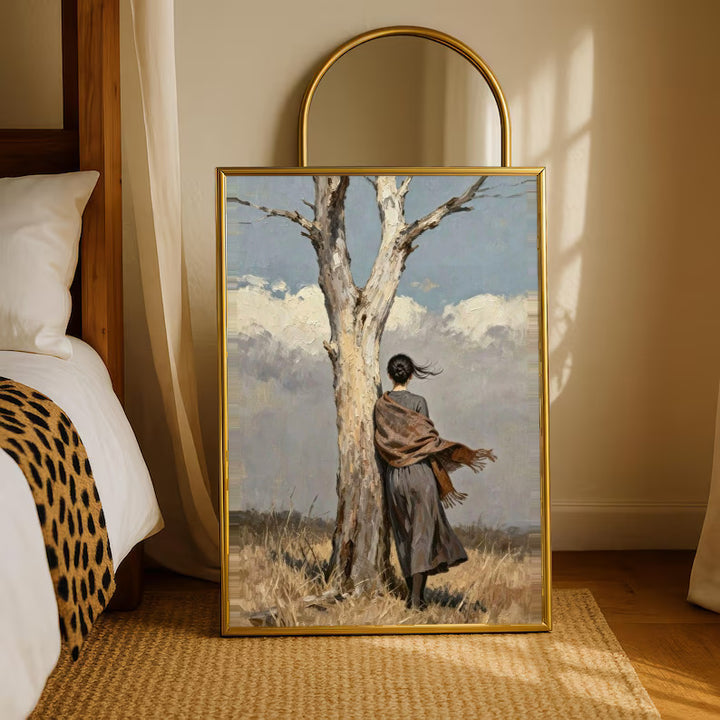 A woman in a long dark dress and brown shawl beside a pale tree in a windswept field in a gold-tone styling frame leaning beside a bedroom mirror